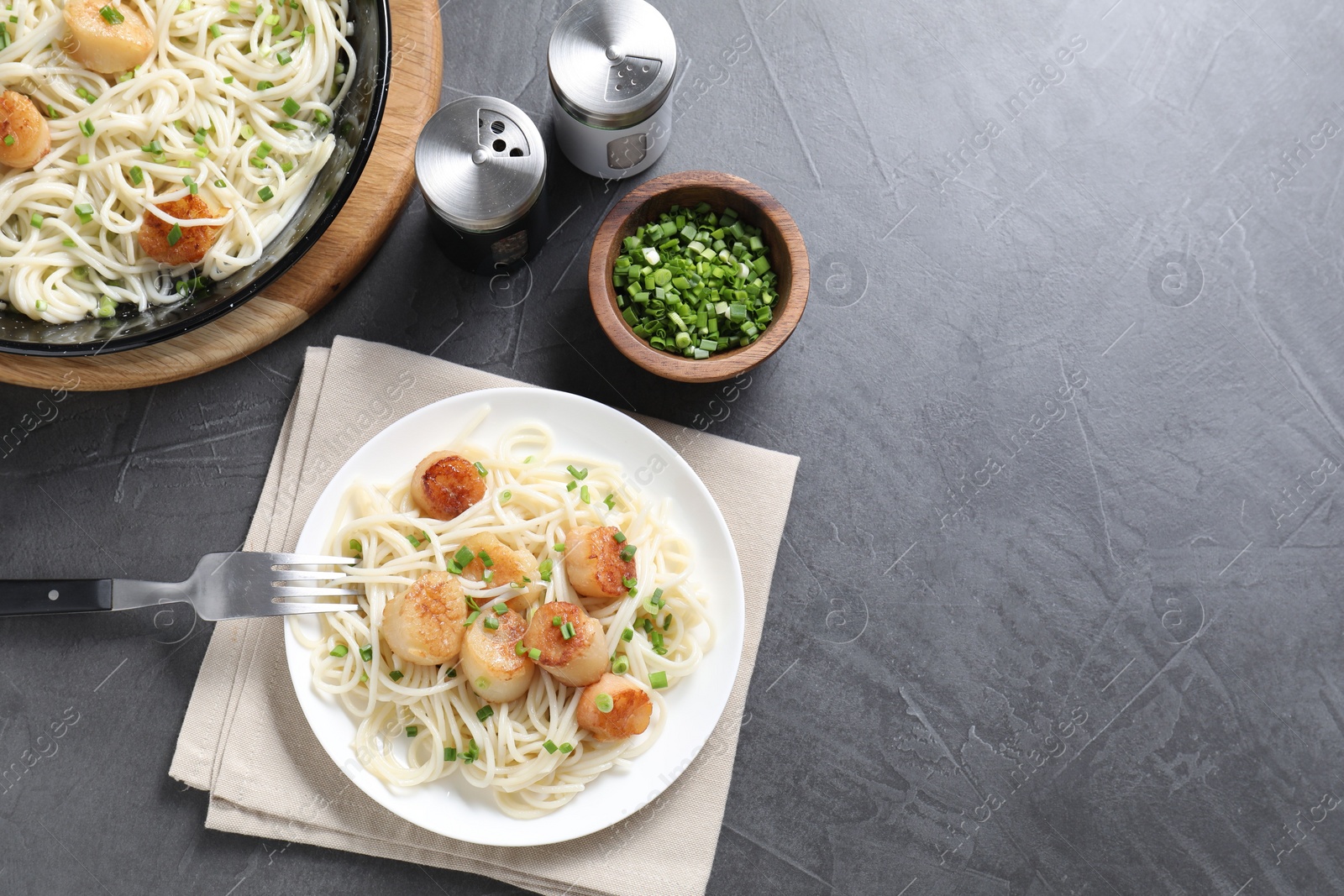 Photo of Delicious scallop pasta with green onion served on grey table, flat lay. Space for text