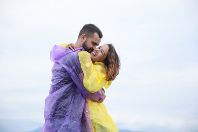 Photo of Young couple in raincoats enjoying time together under rain outdoors, space for text