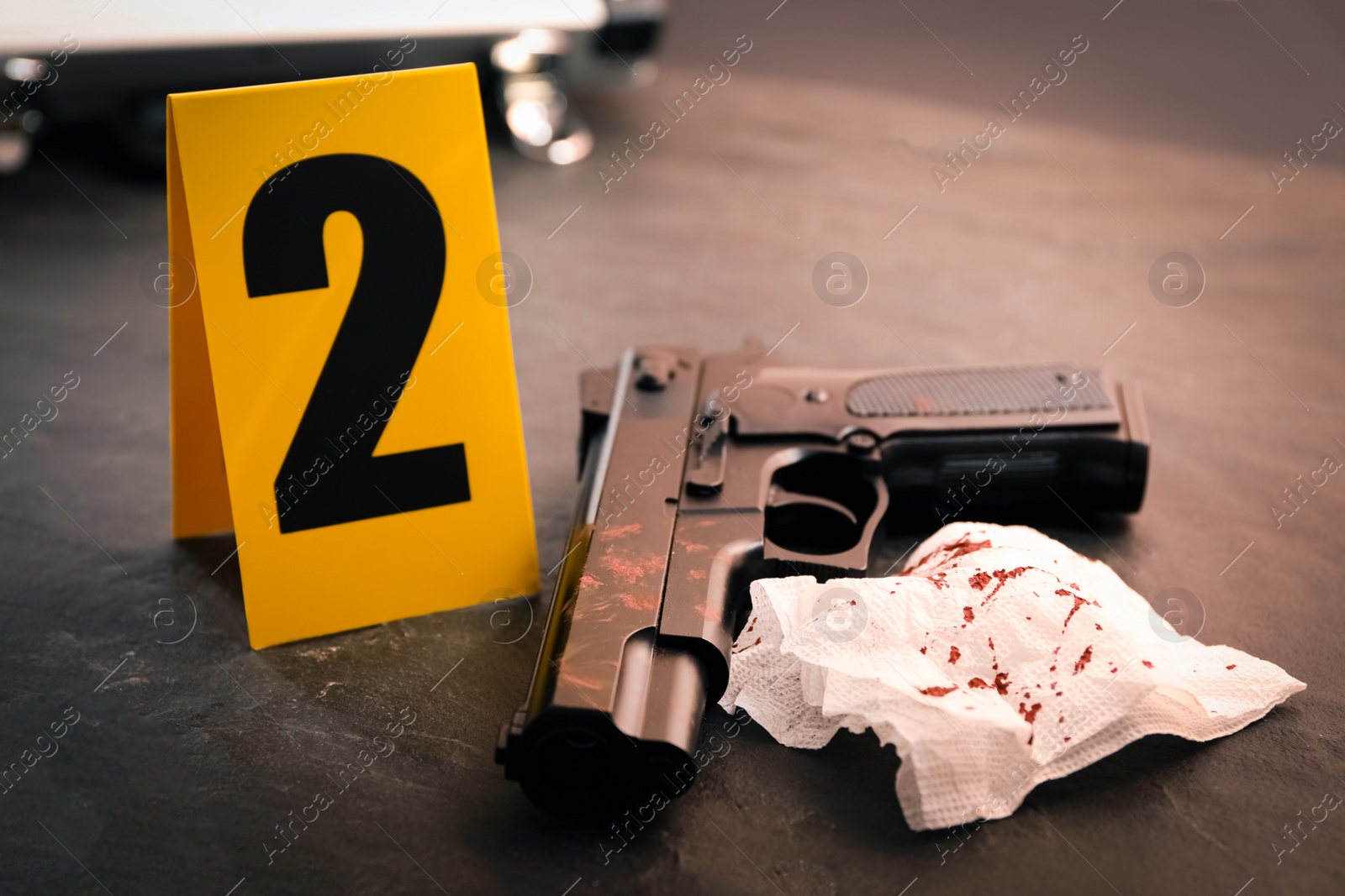 Photo of Napkin with blood, gun and evidence marker on black slate table, closeup. Crime scene