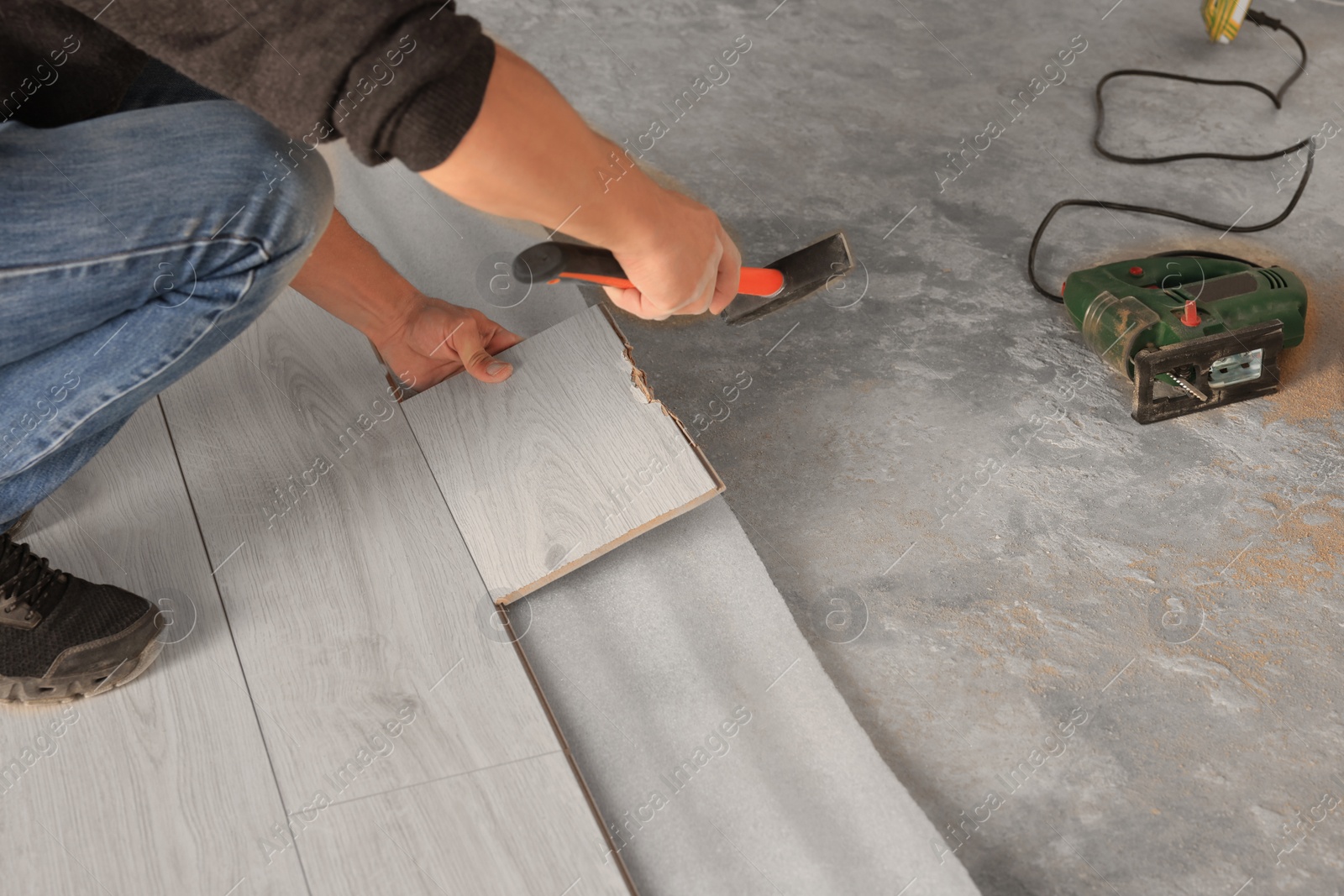 Photo of Professional worker using hammer during installation of new laminate flooring, closeup