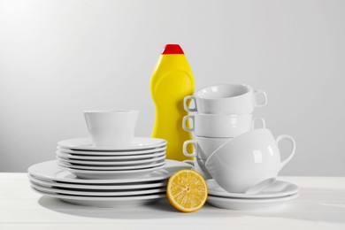 Clean tableware, dish detergent and half of lemon on white wooden table against light background