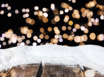 Image of Wooden surface with heap of snow and blurred Christmas lights on background, bokeh effect 