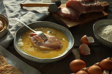 Cooking schnitzel. Raw pork chop in eggs, meat mallet and ingredients on wooden table