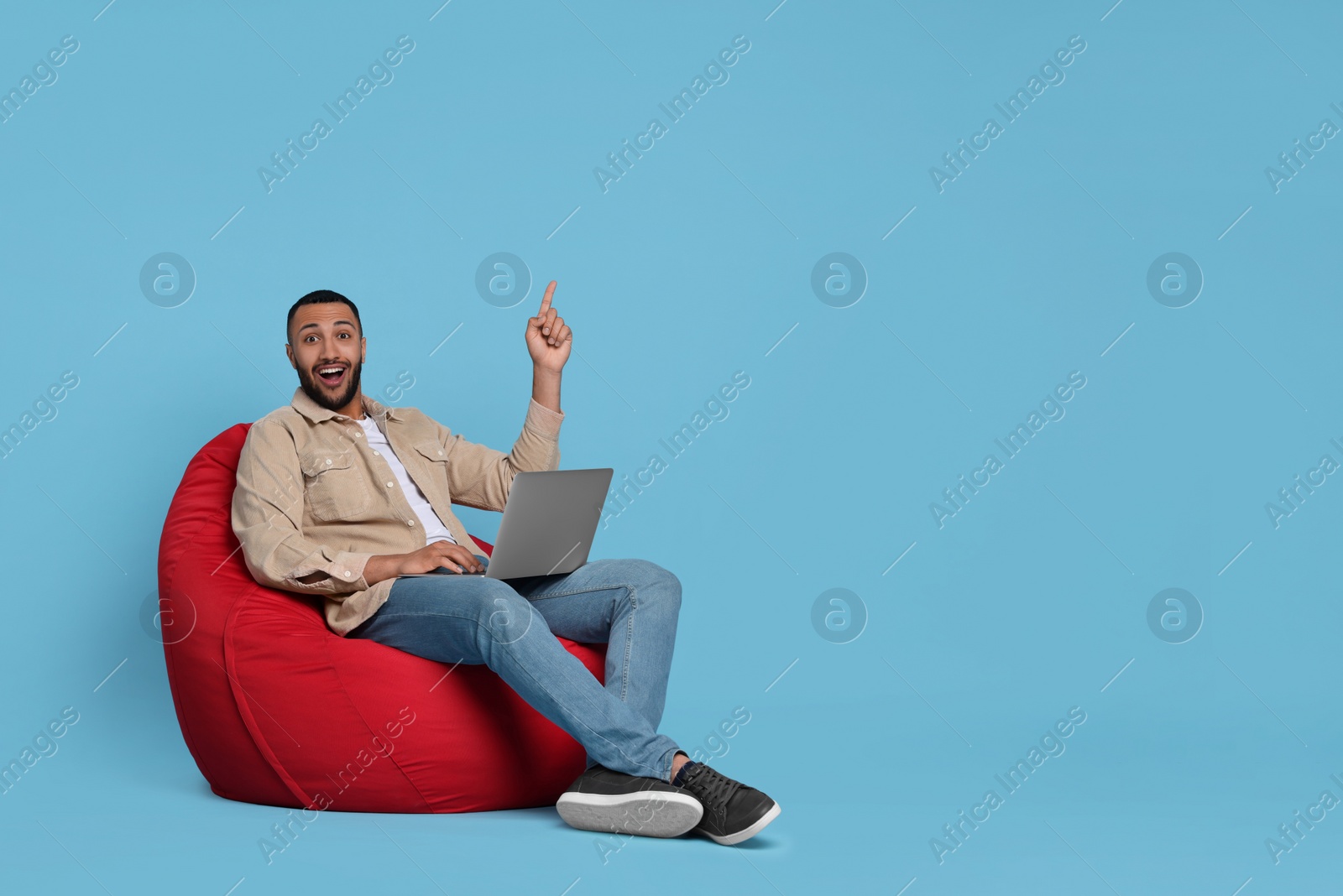 Photo of Smiling young man with laptop sitting on beanbag chair against light blue background