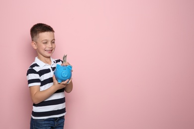 Photo of Little boy putting money into piggy bank on color background. Space for text