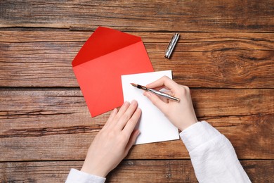 Woman writing letter at wooden table, top view