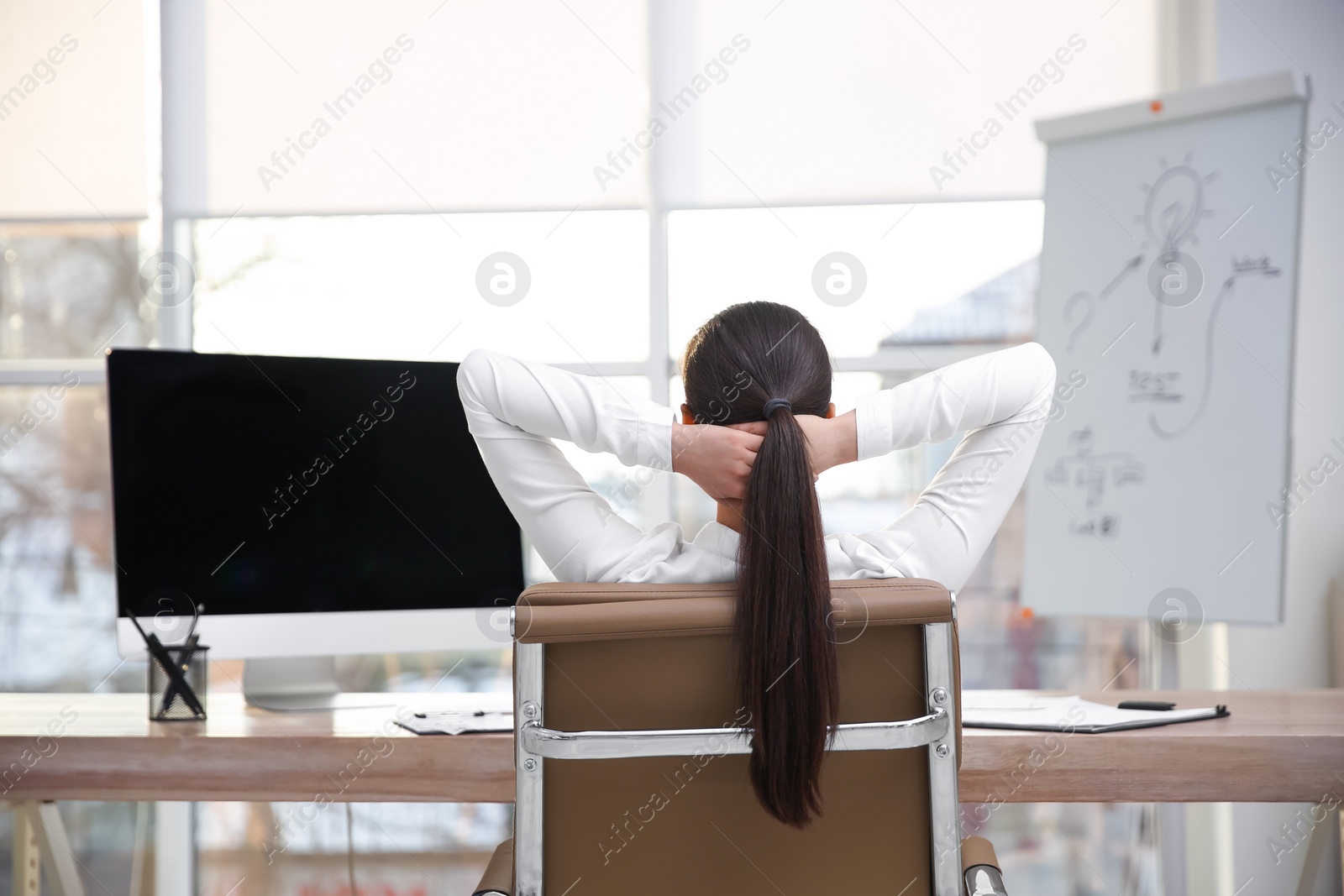 Photo of Young woman relaxing in office chair at workplace, back view