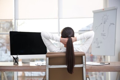 Photo of Young woman relaxing in office chair at workplace, back view