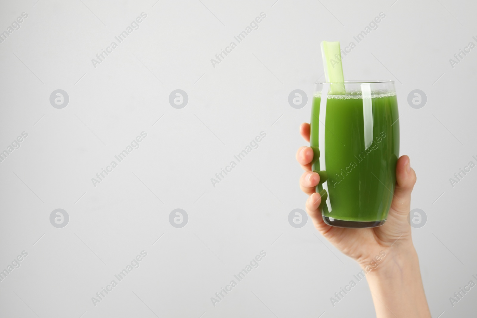 Photo of Woman holding glass of delicious celery juice on light grey background, closeup. Space for text