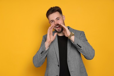 Handsome man in stylish grey jacket screaming on yellow background