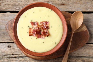 Photo of Tasty potato soup with bacon in bowl and spoon on wooden table, flat lay