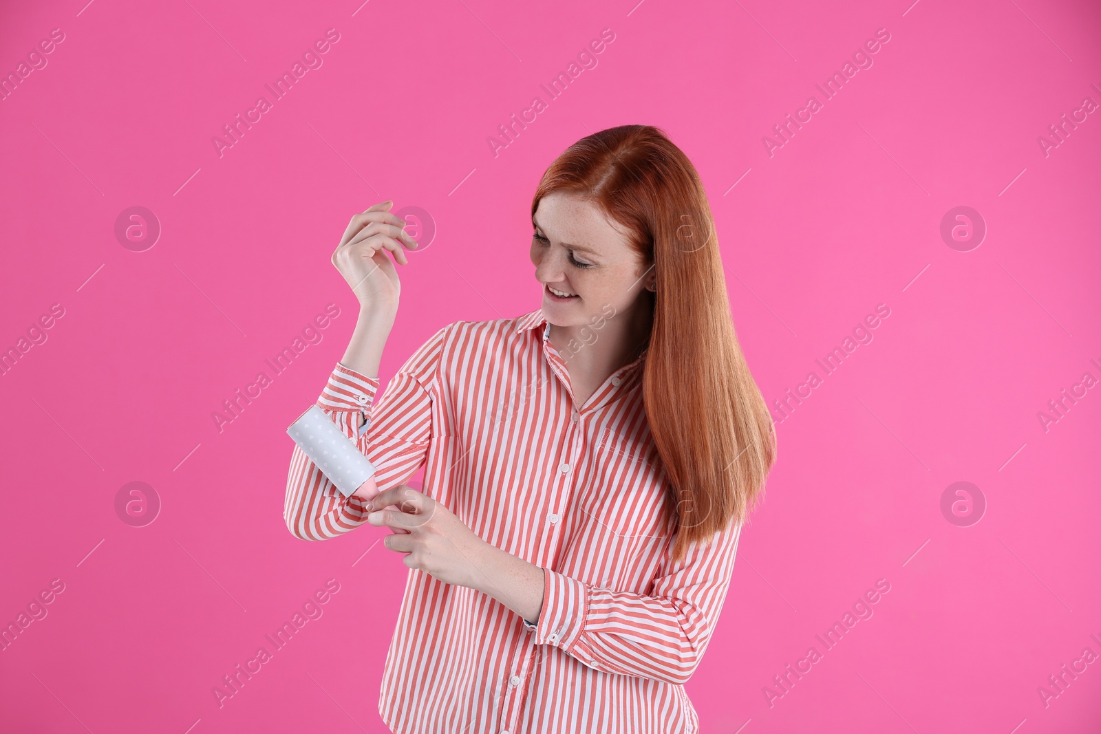 Photo of Young woman cleaning clothes with lint roller on pink background