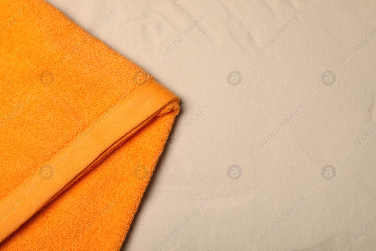 Photo of Orange beach towel on sand, top view. Space for text