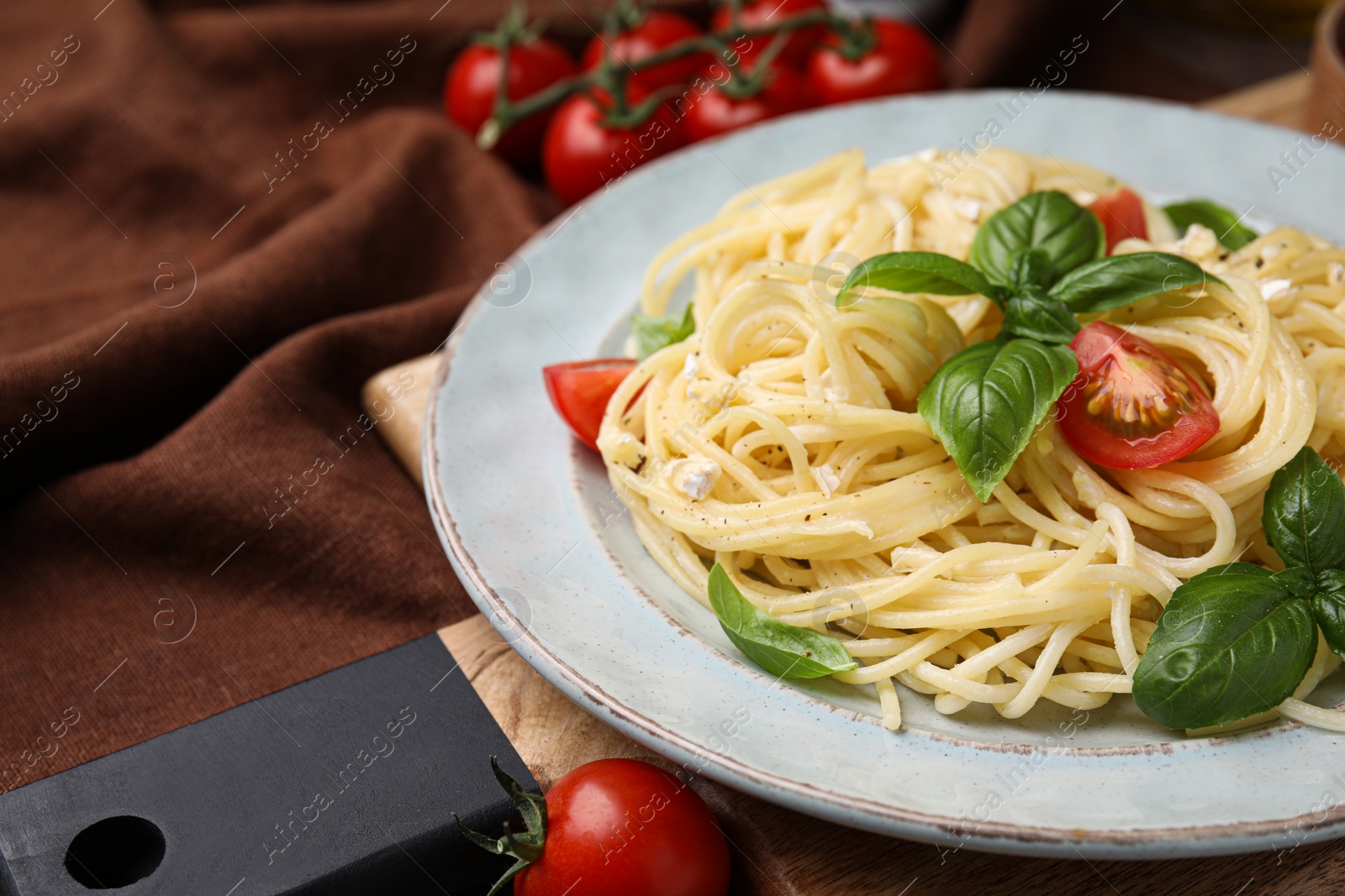 Photo of Delicious pasta with brie cheese, tomatoes and basil leaves on brown tablecloth, closeup. Space for text