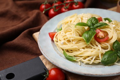 Photo of Delicious pasta with brie cheese, tomatoes and basil leaves on brown tablecloth, closeup. Space for text