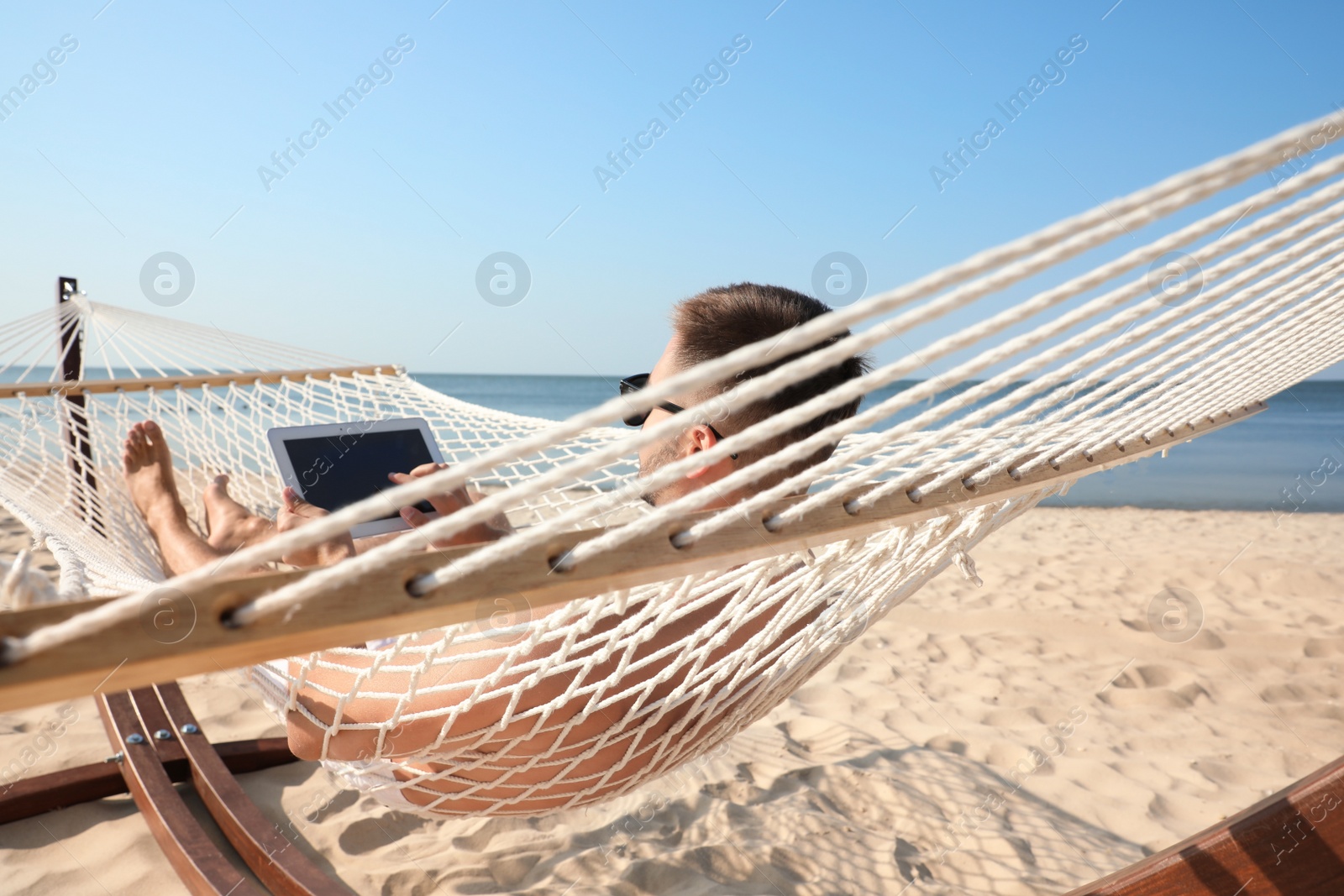 Photo of Young man with tablet in hammock on beach