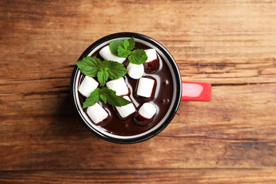 Mug of delicious hot chocolate with marshmallows and fresh mint on wooden table, top view