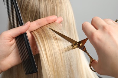 Hairdresser cutting client's hair with scissors on light grey background, closeup