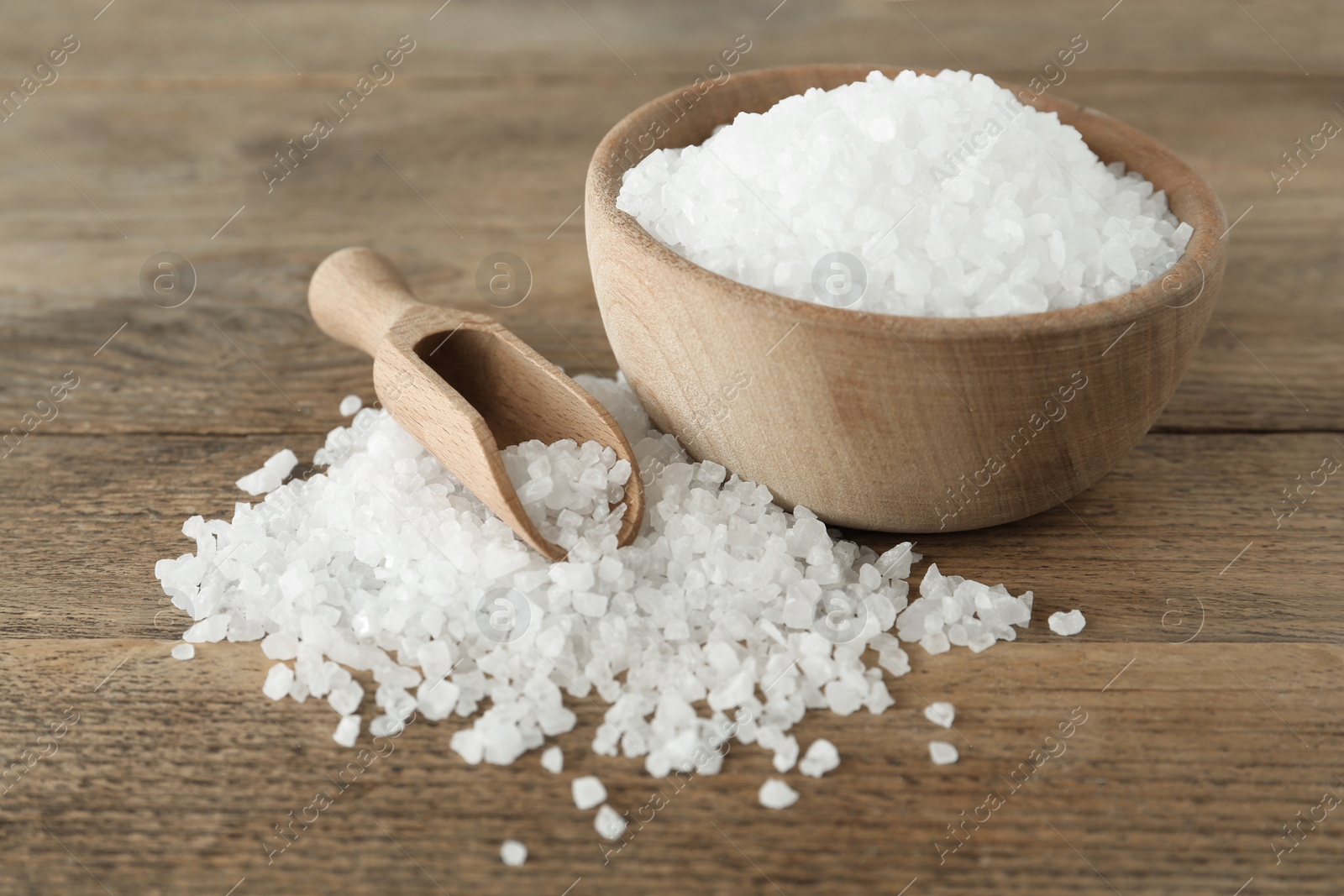 Photo of Natural sea salt, bowl and scoop on wooden table