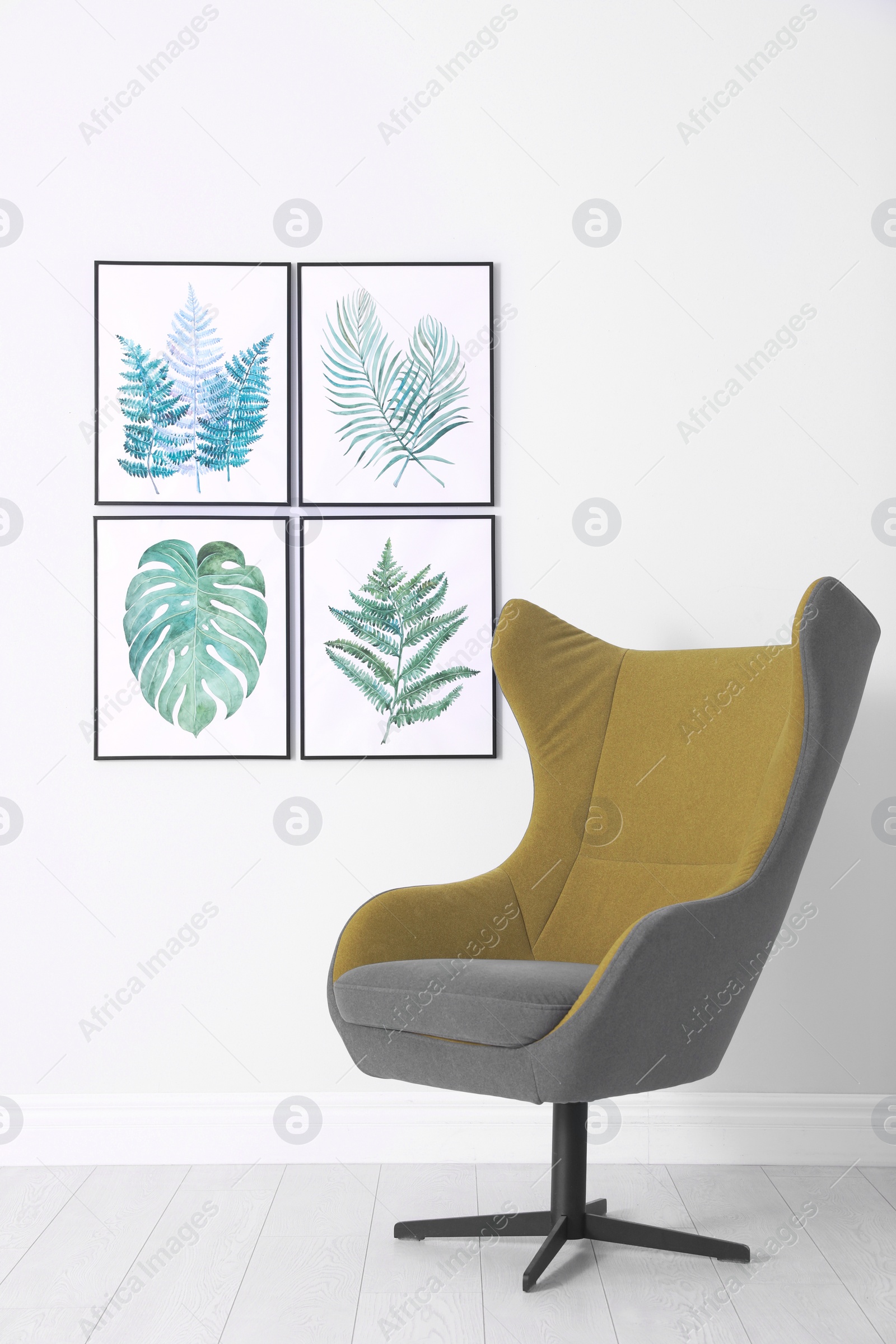 Photo of Stylish comfortable armchair and paintings of tropical leaves. Interior design