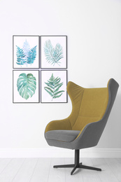 Photo of Stylish comfortable armchair and paintings of tropical leaves. Interior design