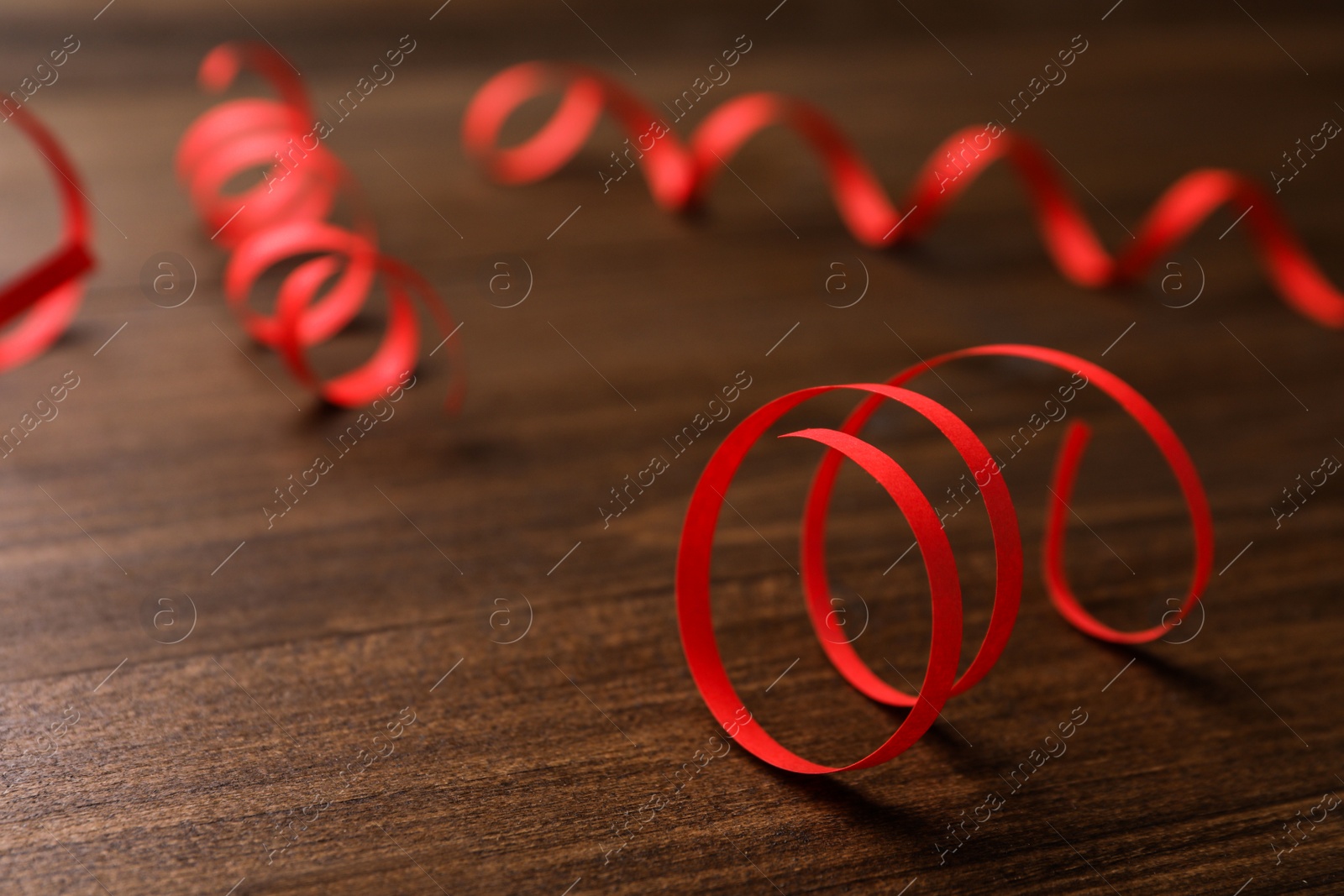 Photo of Red serpentine streamers on wooden table. Space for text