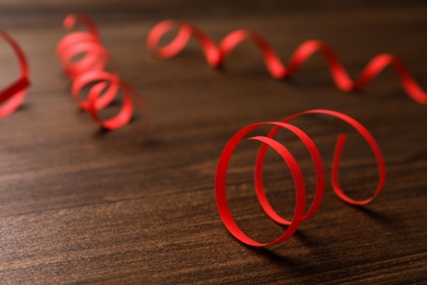 Photo of Red serpentine streamers on wooden table. Space for text