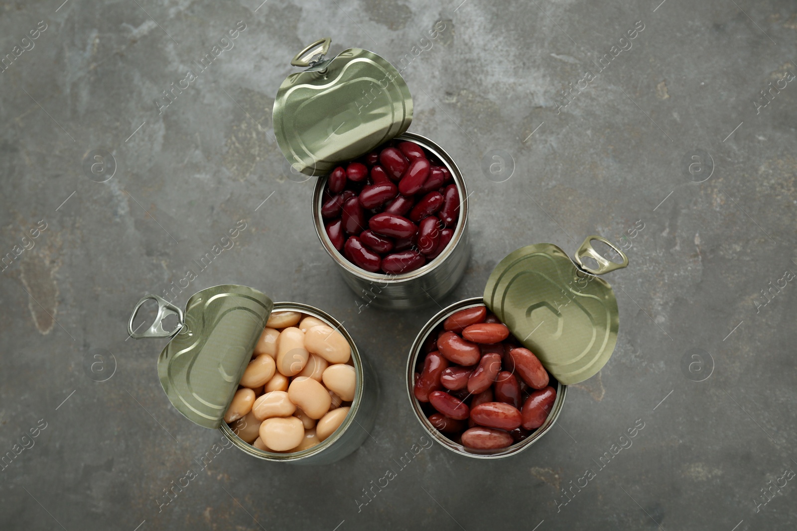 Photo of Tin cans with different canned kidney beans on grey table, flat lay