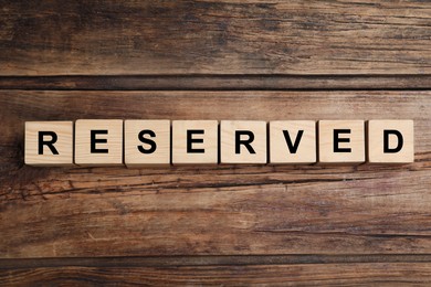 Photo of Word RESERVED made with cubes on wooden surface, top view. Table setting element