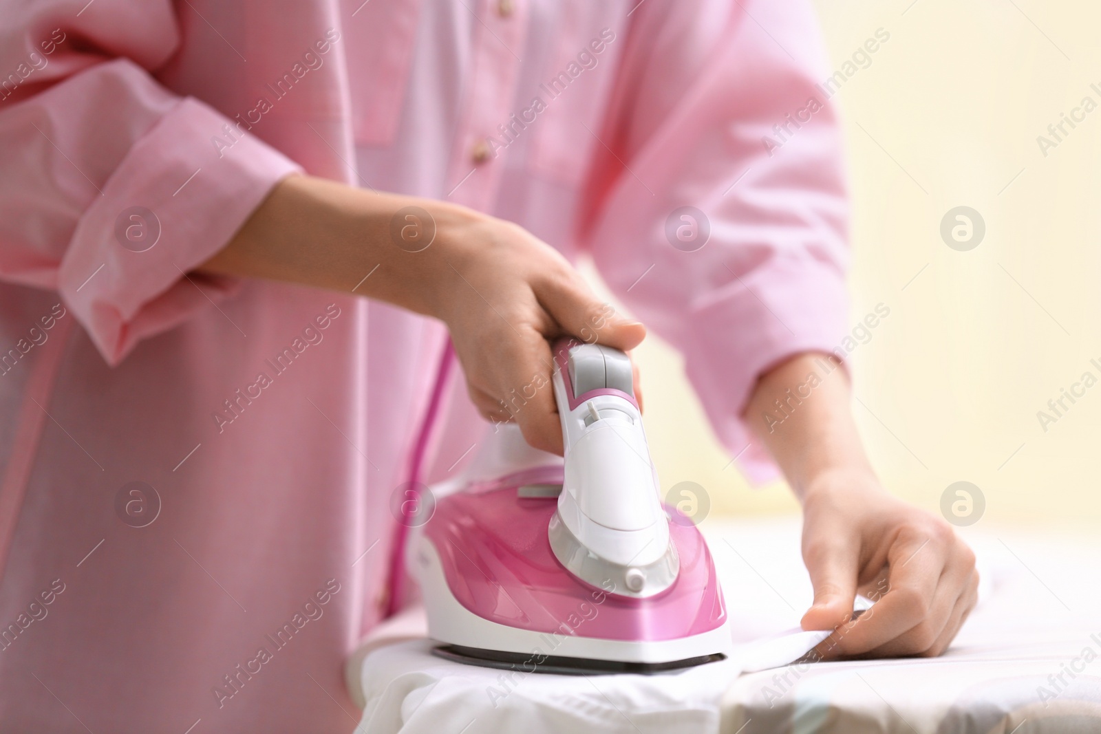 Photo of Woman ironing shirt on board indoors, closeup