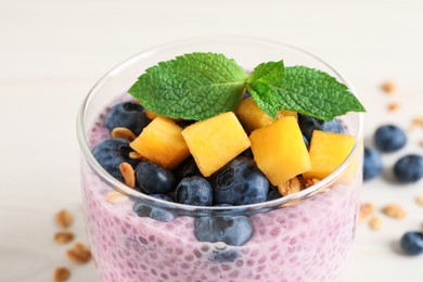 Photo of Delicious chia pudding with blueberries, mango and mint in glass on white table, closeup