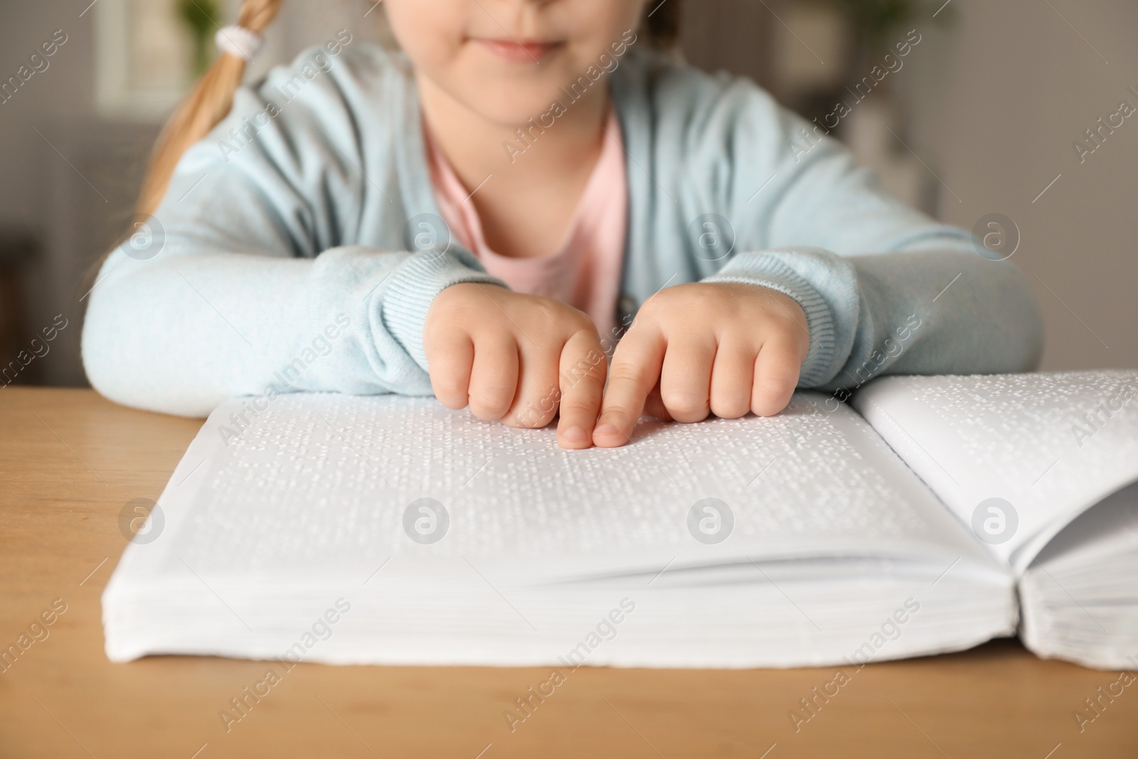 Photo of Blind child reading book written in Braille at table, closeup