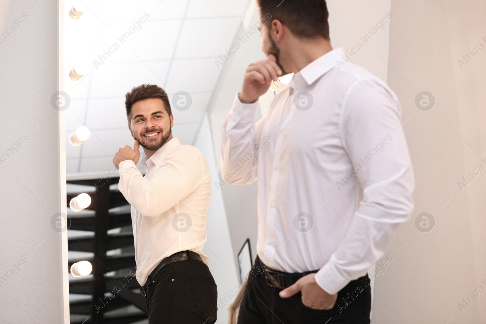 Photo of Young man looking at himself in large mirror at home