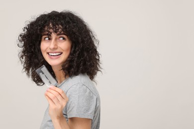 Photo of Young woman holding teeth whitening strips on light grey background, space for text