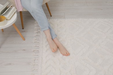 Photo of Woman sitting on armchair near beige carpet indoors, closeup