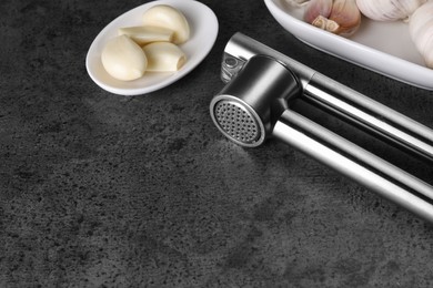 Photo of Garlic press and cloves on grey table. Space for text