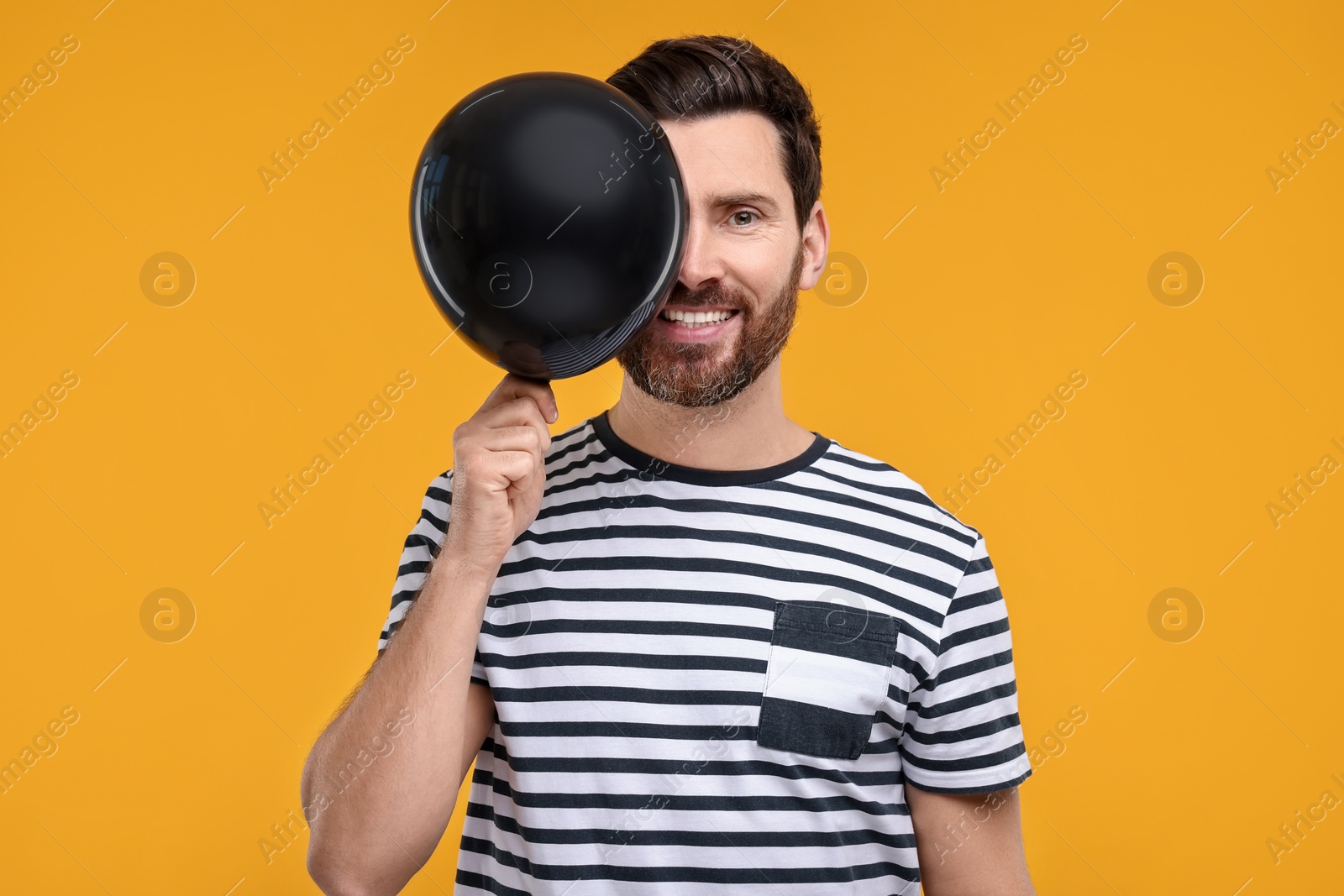 Photo of Happy man with black balloon on yellow background
