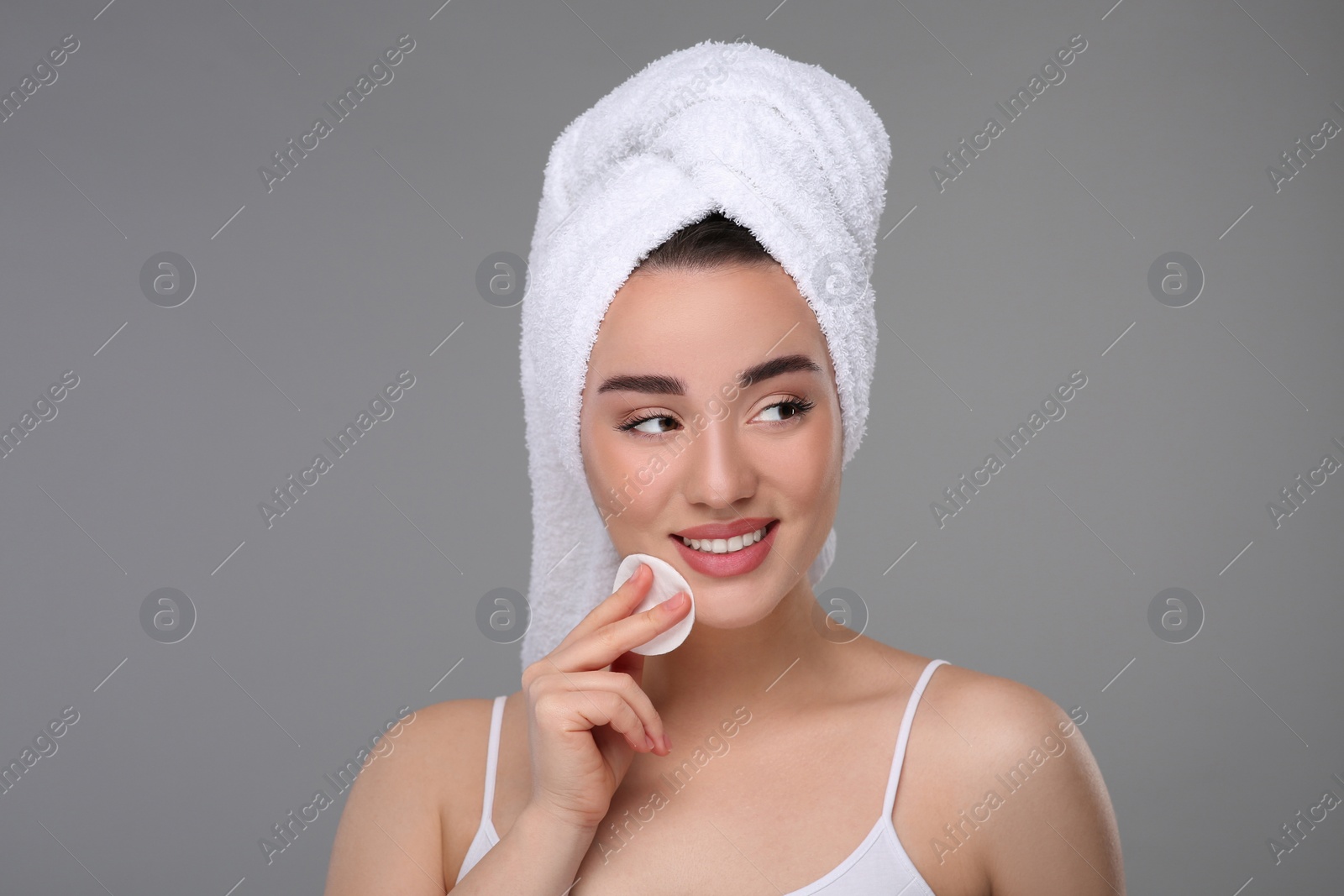 Photo of Beautiful woman in terry towel removing makeup with cotton pad on gray background