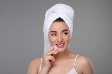 Beautiful woman in terry towel removing makeup with cotton pad on gray background