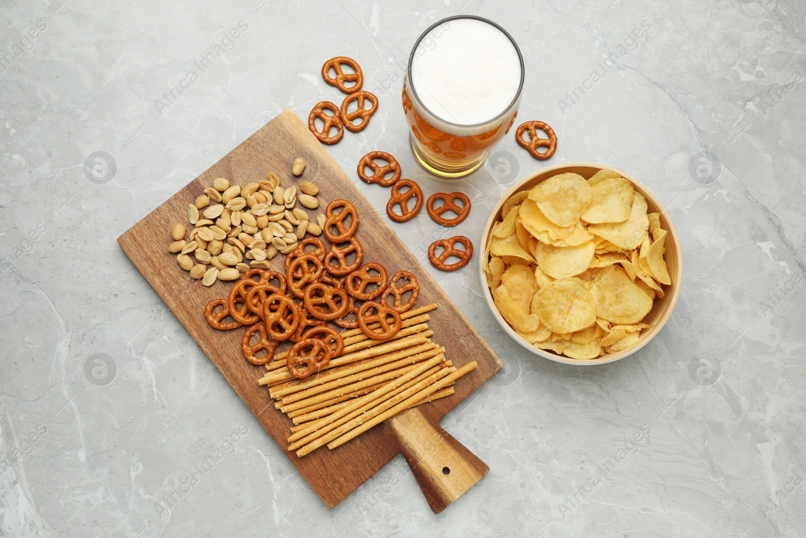 Photo of Glass of beer served with delicious pretzel crackers and other snacks on light grey table, flat lay