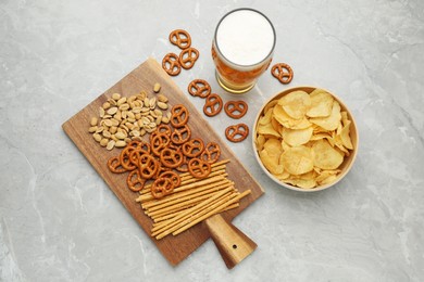 Photo of Glass of beer served with delicious pretzel crackers and other snacks on light grey table, flat lay