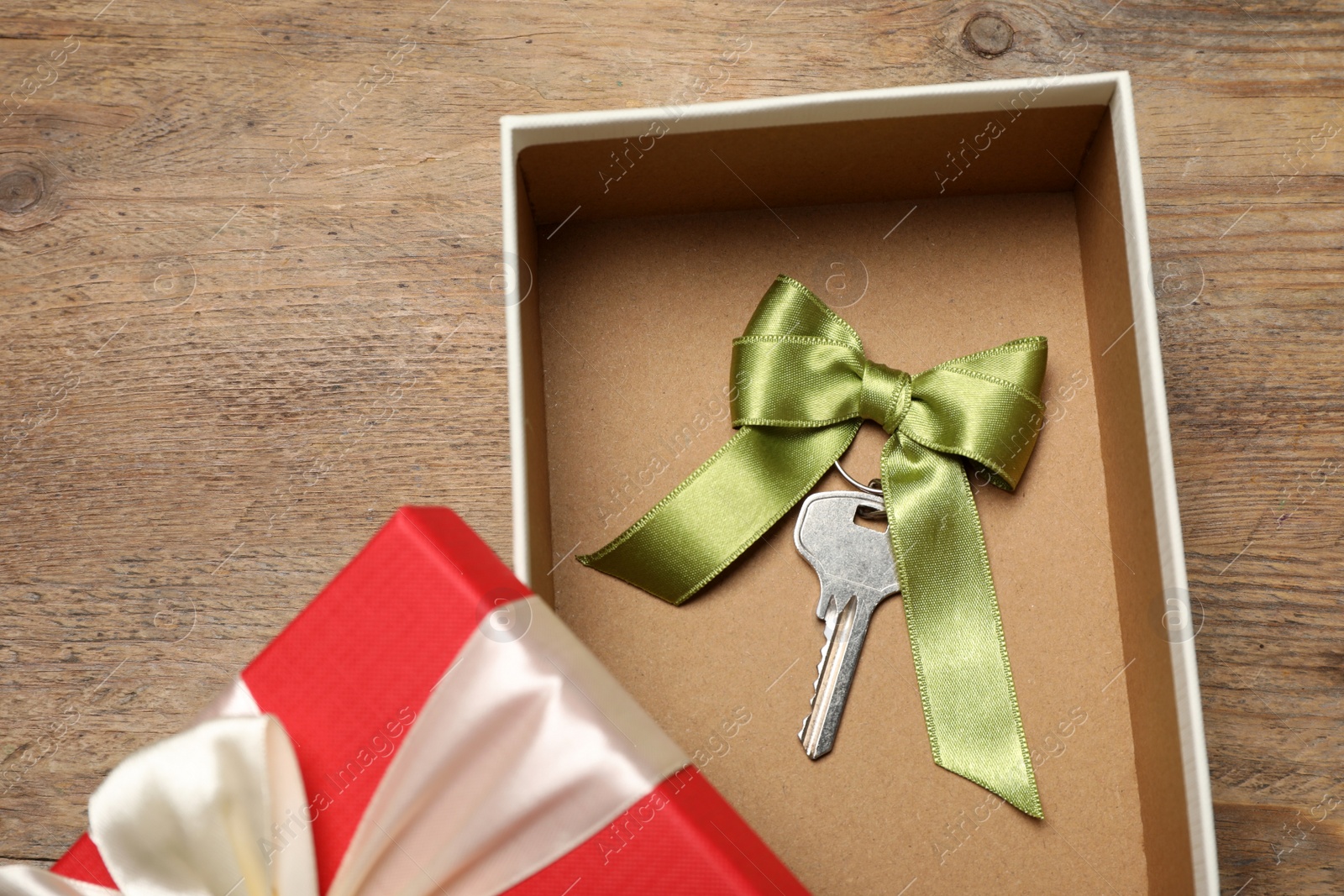 Photo of Key with bow in gift box on wooden table, top view. Housewarming party