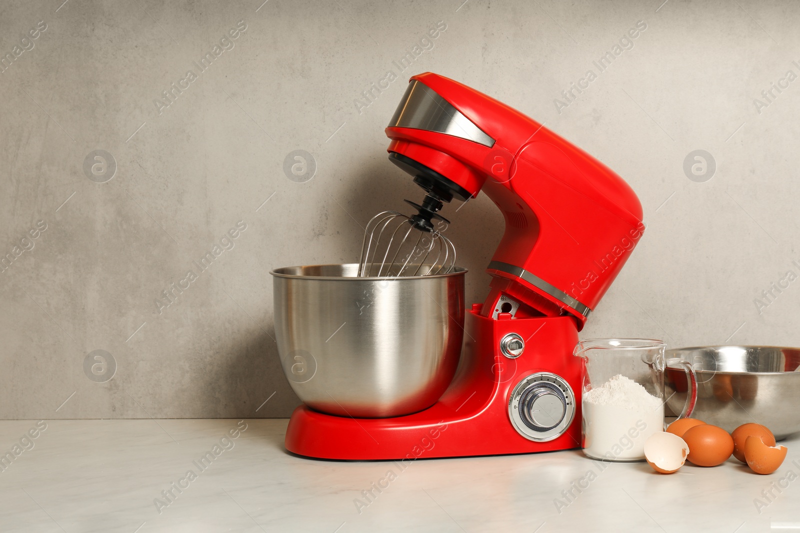 Photo of Modern red stand mixer, eggs, container with flour and bowl on white marble table. Space for text