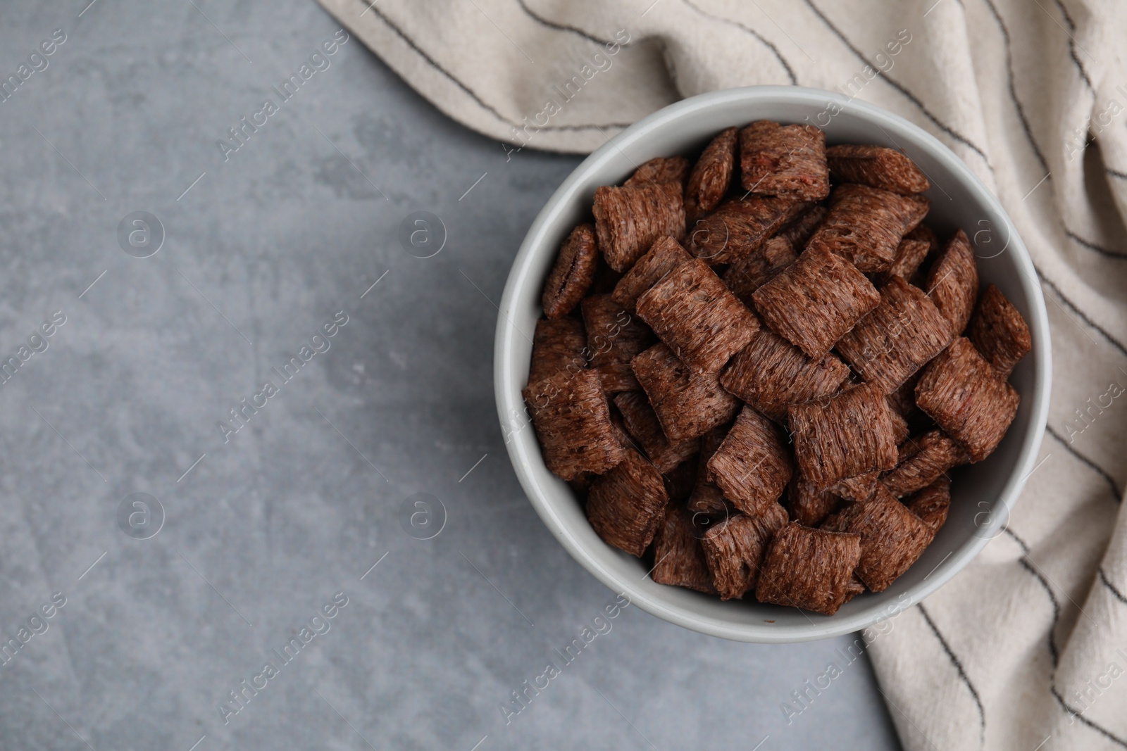 Photo of Chocolate cereal pads in bowl on grey table, top view. Space for text