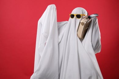 Person in ghost costume and sunglasses using retro radio receiver on red background, space for text