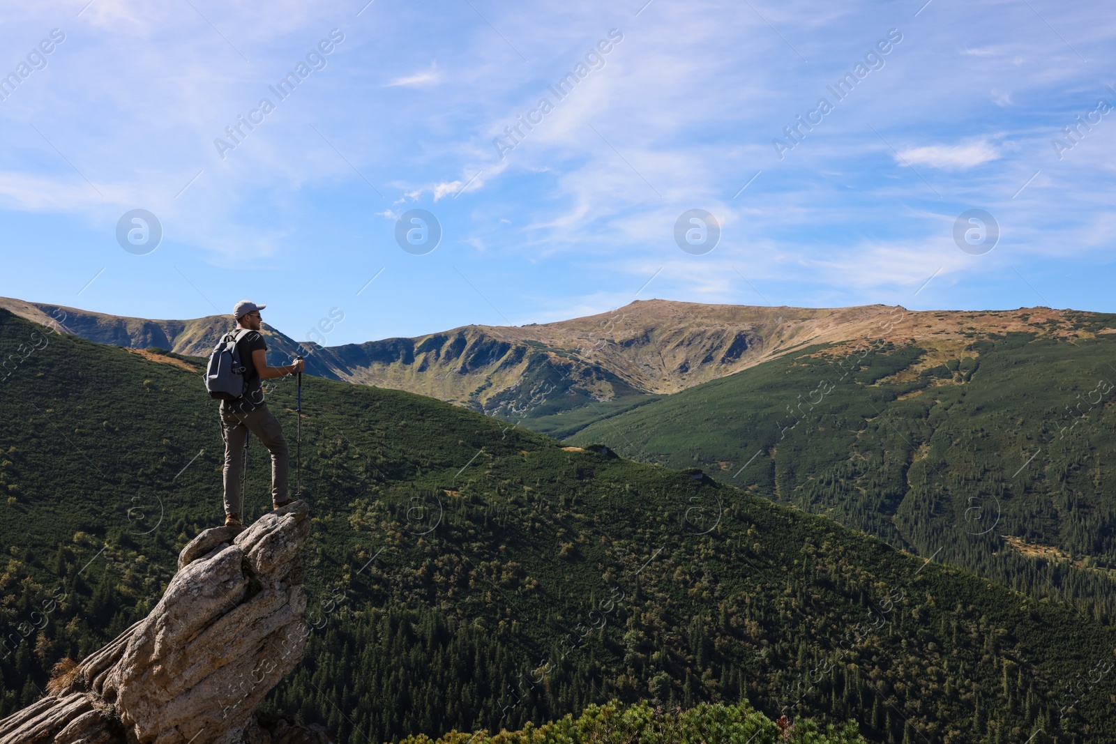 Photo of Man with trekking poles enjoying picturesque view on cliff in mountains. Space for text