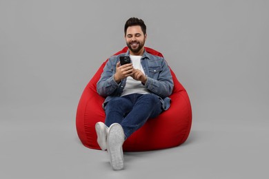 Photo of Happy young man using smartphone on bean bag chair against grey background