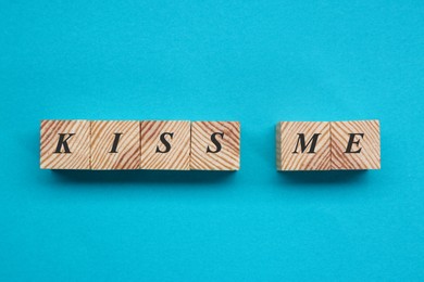 Photo of Wooden cubes with phrase Kiss Me on light blue background, flat lay