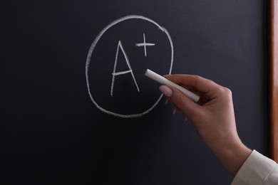 School grade. Teacher writing letter A and plus symbol with chalk on blackboard, closeup