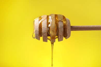 Delicious honey flowing down from dipper against yellow background, closeup